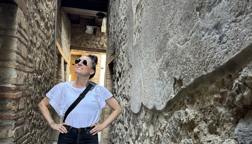 Kristen Mallia wears sunglasses as she stands between the walls of an Italian ruin